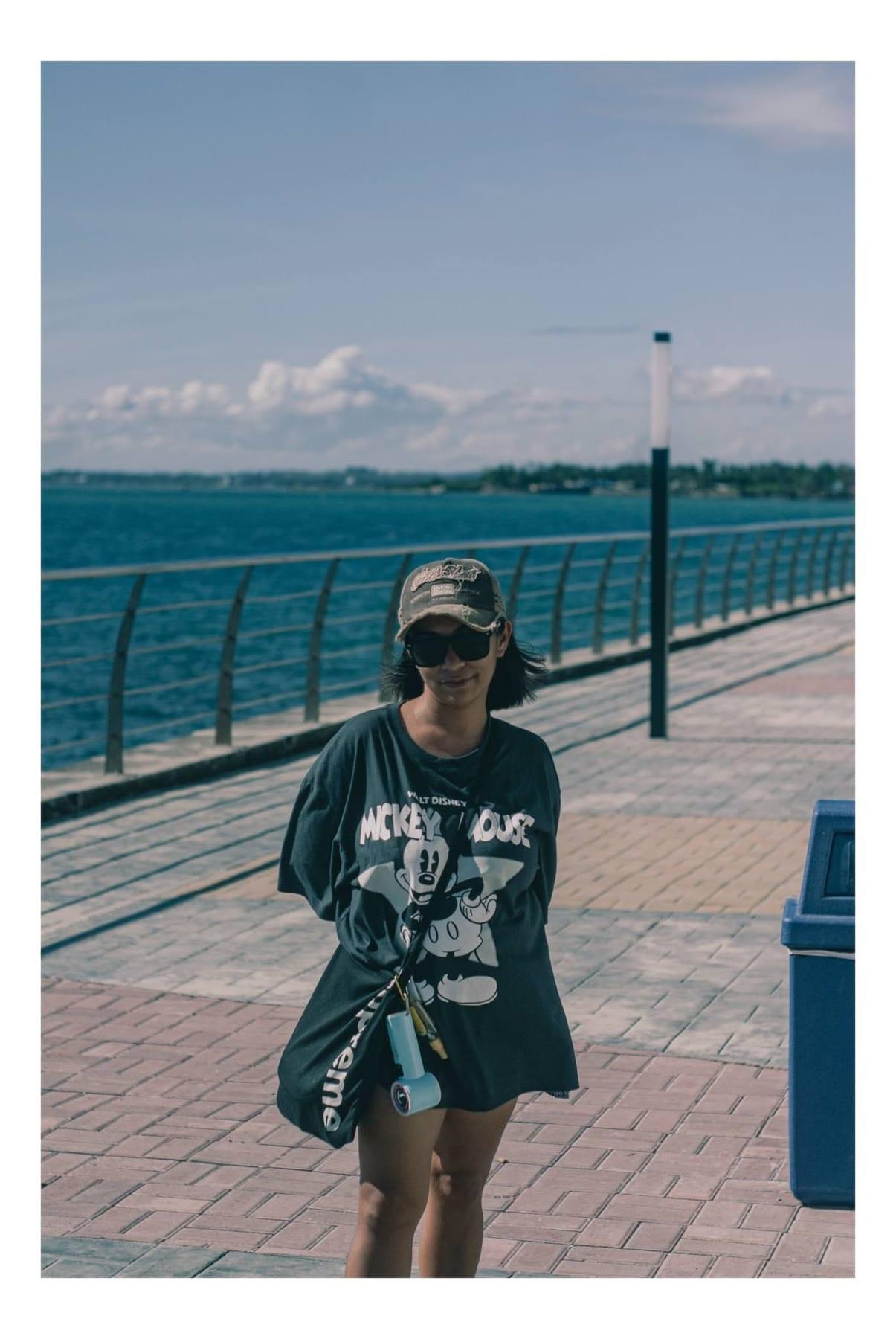 Woman in sunglasses and a graphic t-shirt standing on a sunny seaside boardwalk