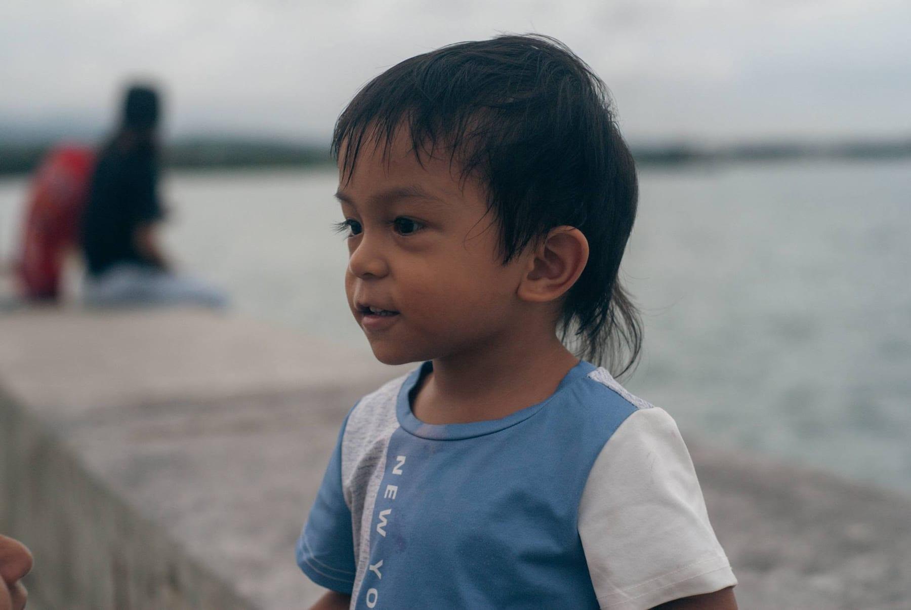 Candid portrait of a young boy looking off-camera near a waterfront on an overcast day