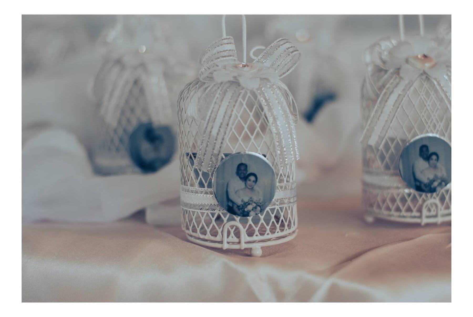 Decorative white wire birdcage wedding favors with ribbon bows and circular couple portraits