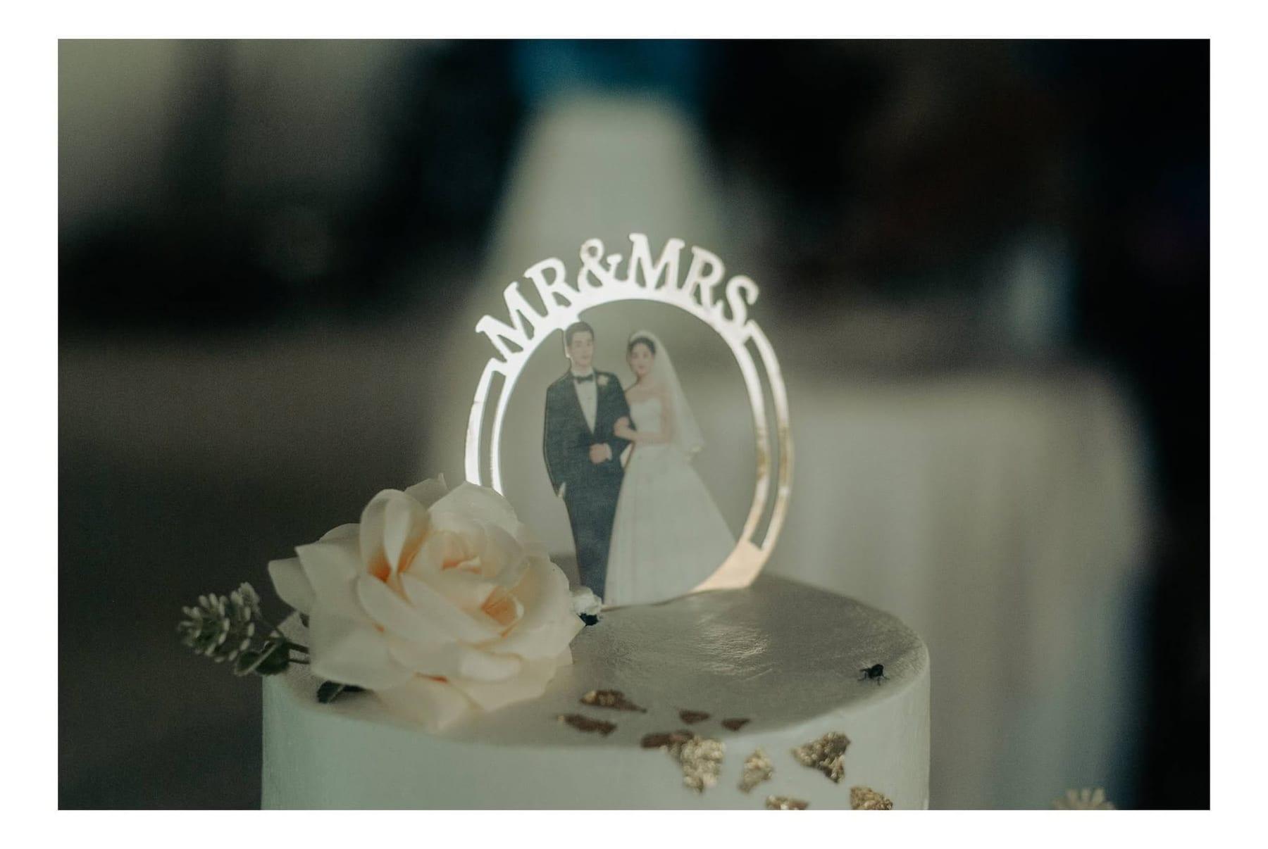 Close-up of a wedding cake with a gold Mr and Mrs topper, gold leaf, and a cream rose
